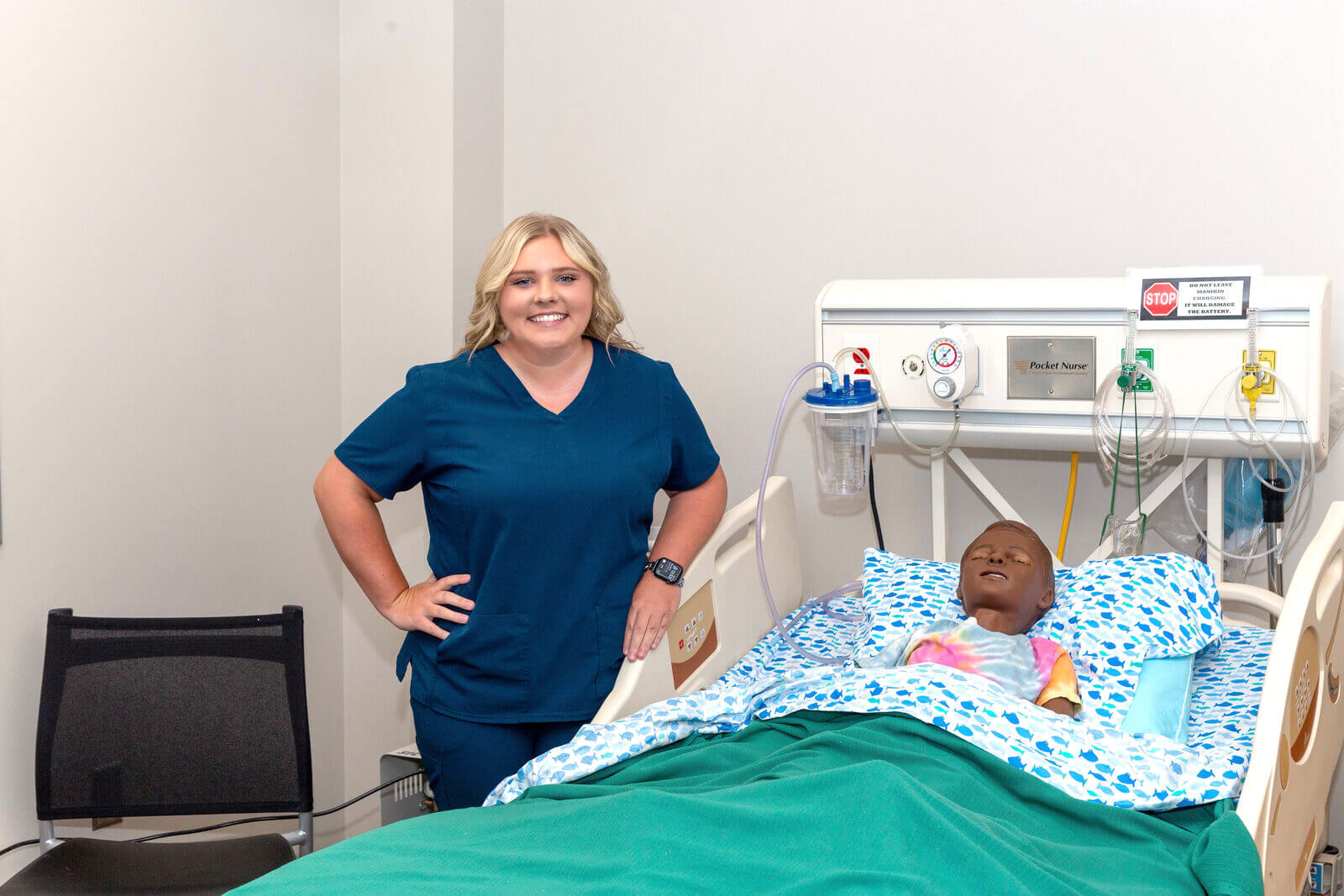 Skylar McIntosh poses beside nursing mannequin in Sim Lab