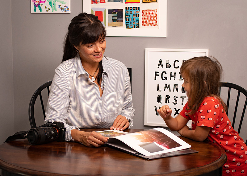 Rose Jerome seated at a round wooden table with her young daughter. they are looking at a photography book. Photo by Zachary Morgan